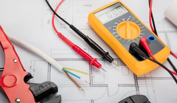 a digital multimeter, cables, and cable cutters resting on a blueprint