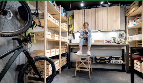 A well-equipped home workshop with bicycles, wooden shelves, and a woman sitting on a workbench