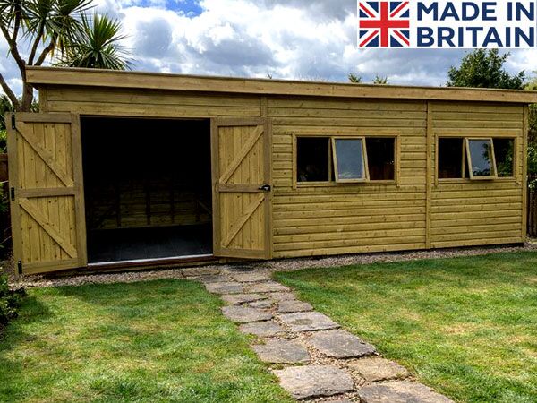 A large garden workshop with large double doors and three windows on the side. The shed has a flat roof and is made of light-coloured wood.